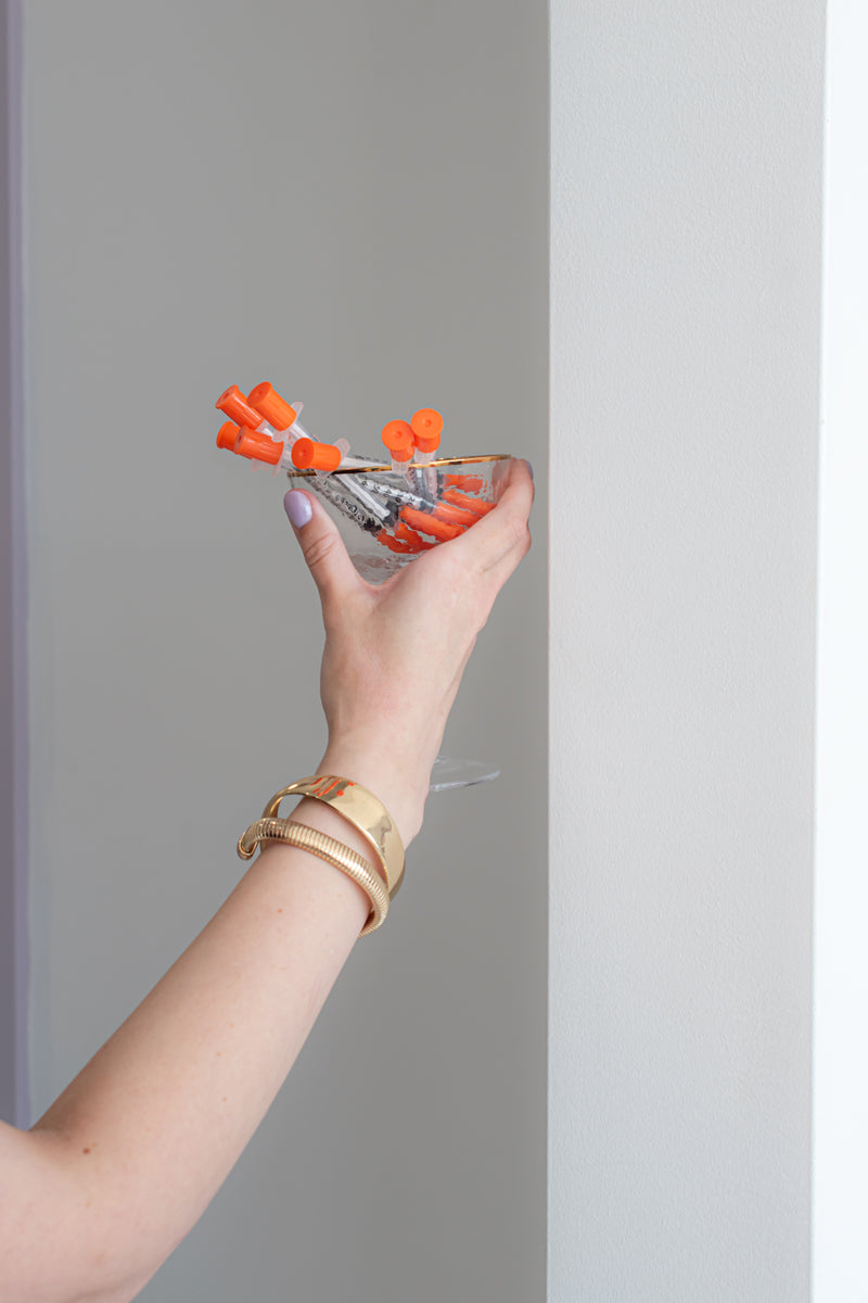 Hand holding a glass with orange candy against a plain background