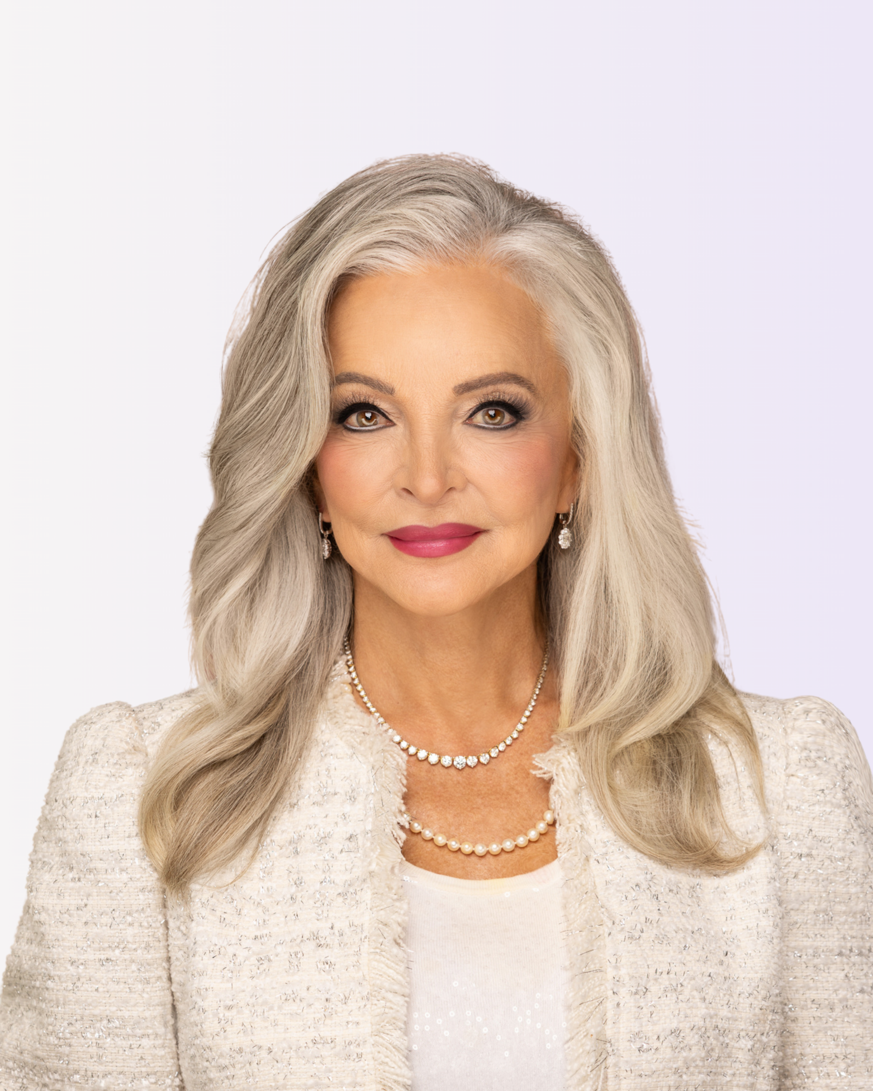 Woman with gray hair wearing a white outfit and pearl necklace on a light purple background
