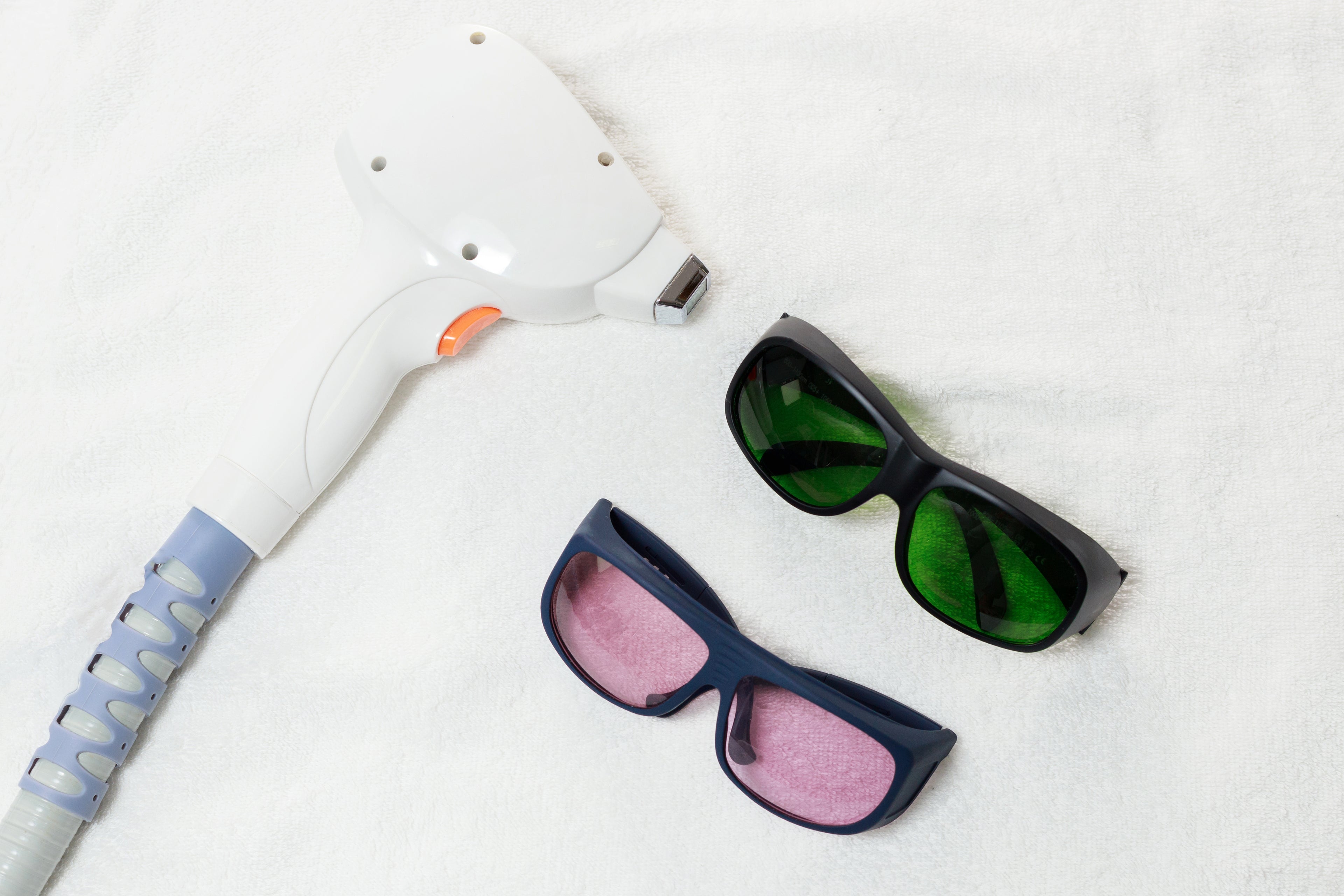 Two pairs of sunglasses and a white device with blue handle on a white background