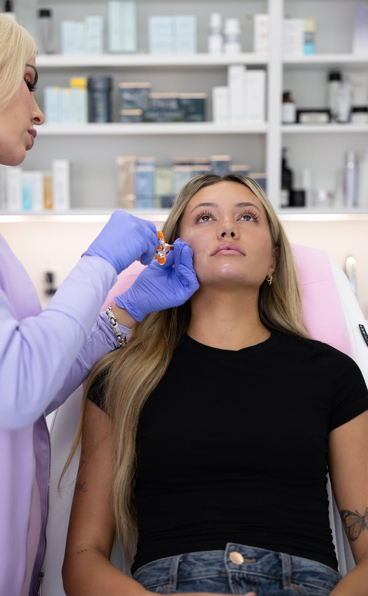 Person getting an ear piercing in a clinical setting with medical equipment in the background.