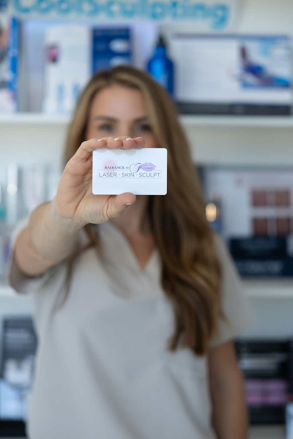 Woman holding a card with 'Radiance at Fluhme Laser Skin Sculpt' in a blurred medical office setting