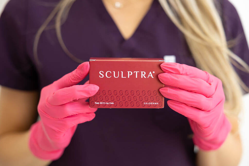 Person wearing pink gloves holding a Sculptra product box. Sculptra treatment t Radiance at Fluhme, Bridgeville, PA