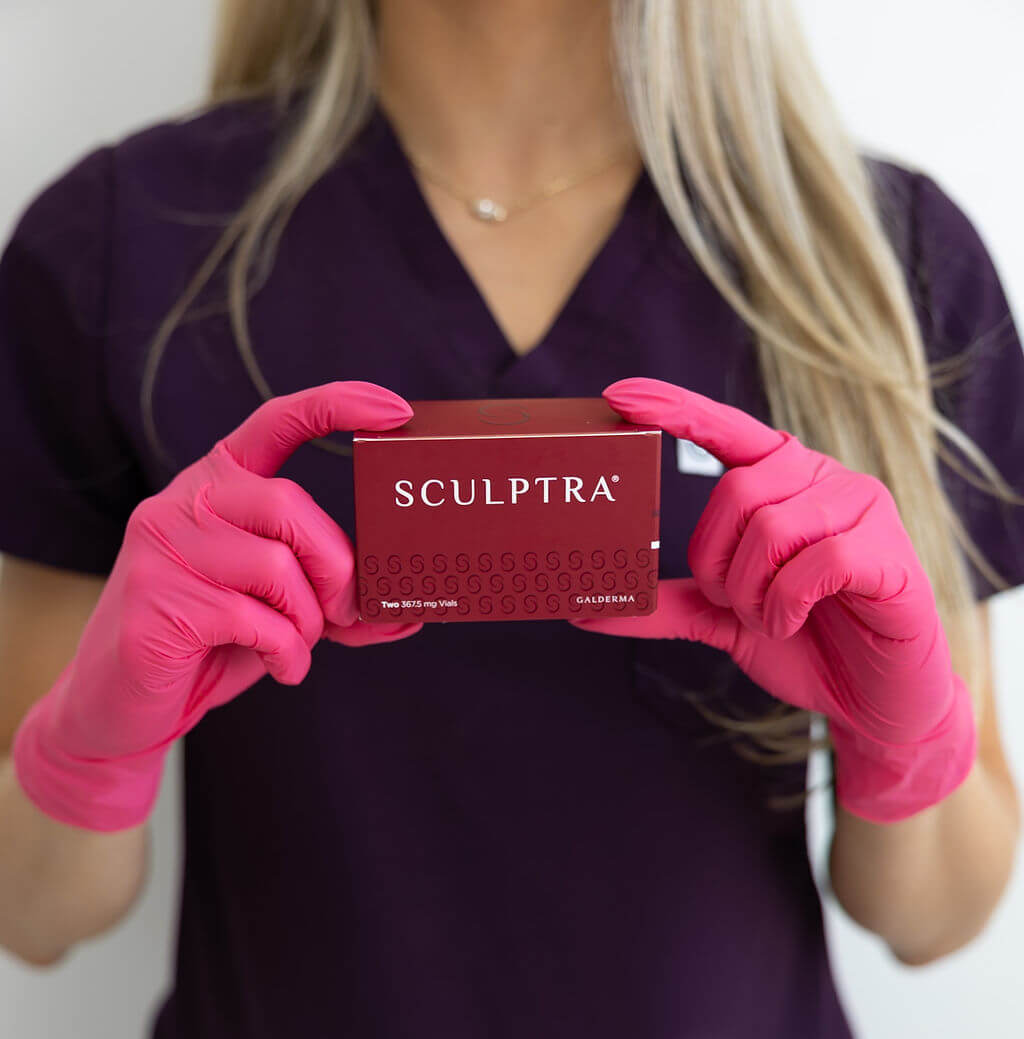 Person wearing pink gloves holding a Sculptra box against a white background