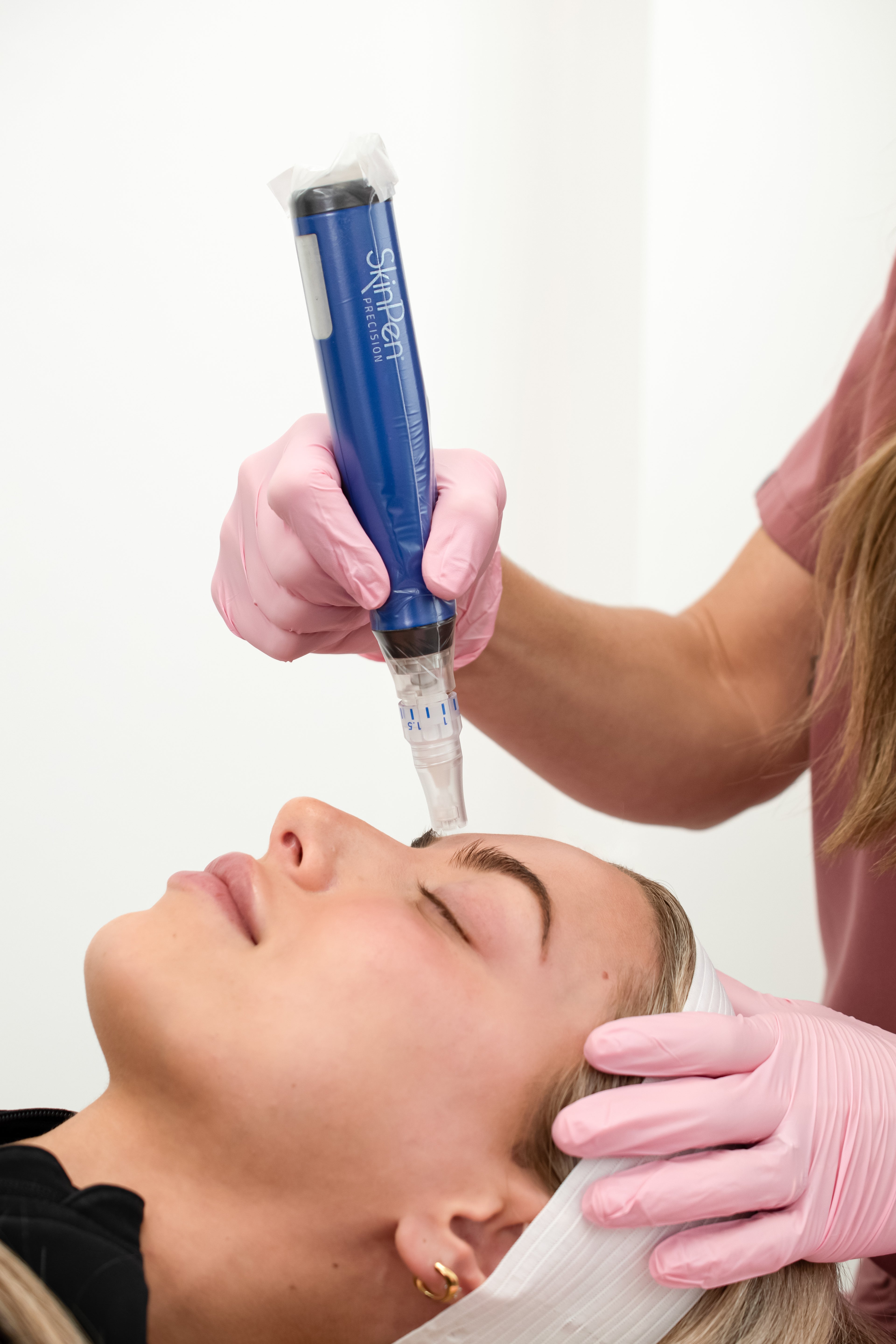 Person receiving a facial treatment with a blue device held by a professional in pink gloves.