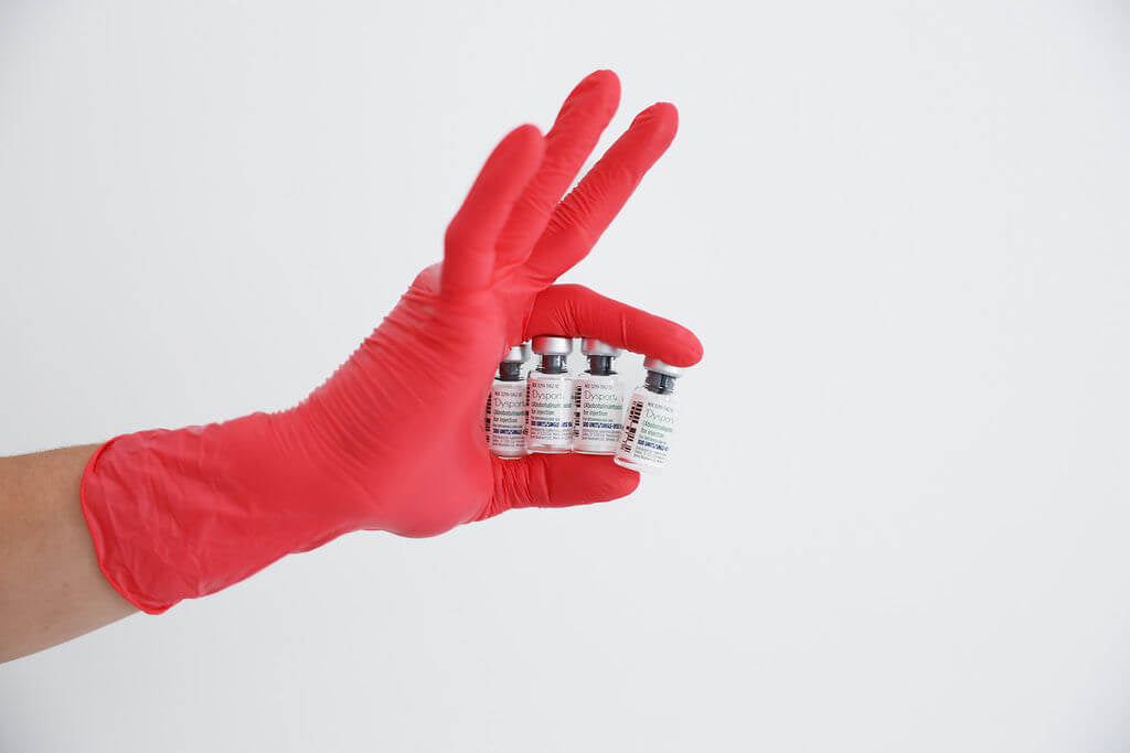 Hand wearing a red glove holding small vials against a white background