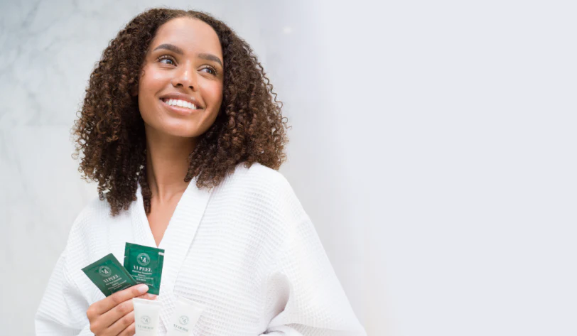 Woman in a white robe holding green packets against a light gray background
