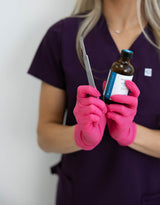Person in purple scrubs and pink gloves holding a bottle and scissors.
